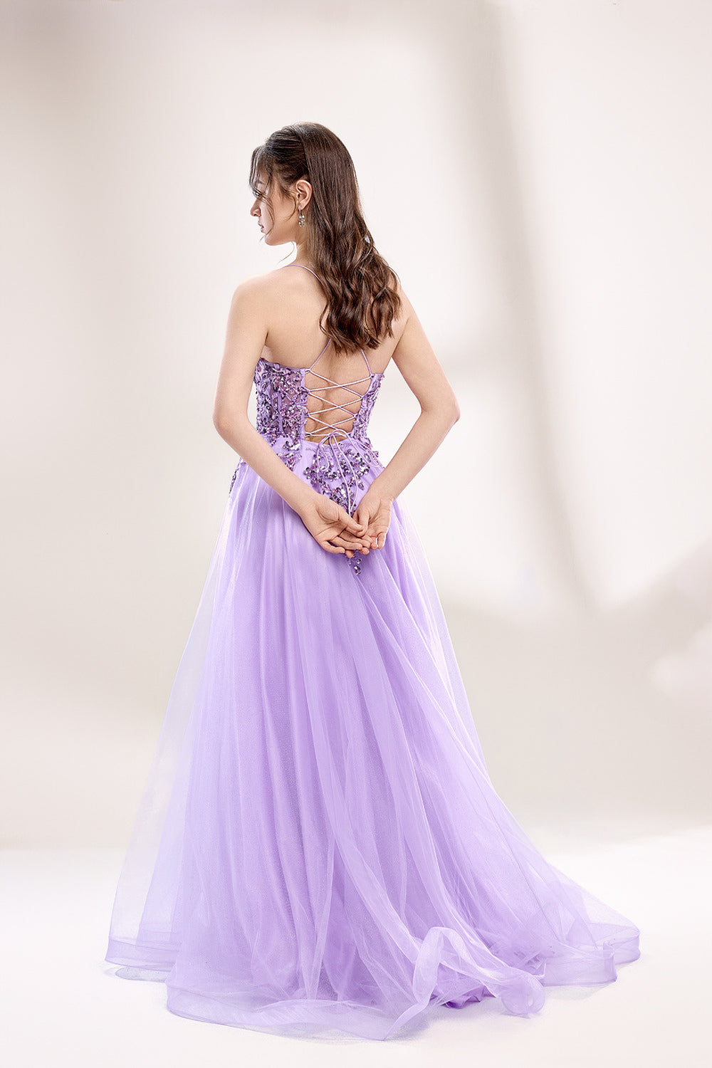 photograph of a young woman wearing a beautiful, floor-length, lavender ball gown with intricate sequin detailing on the bodice, sheer tulle skirt, spaghetti straps, long brown hair, fair skin, standing in a soft lit studio, neutral background, elegant, sophisticated, dreamy, fashion, glamour, full body shot, high quality, fashion photography, stylish, feminine, graceful, classy, modern, delicate, light, airy.33040-02