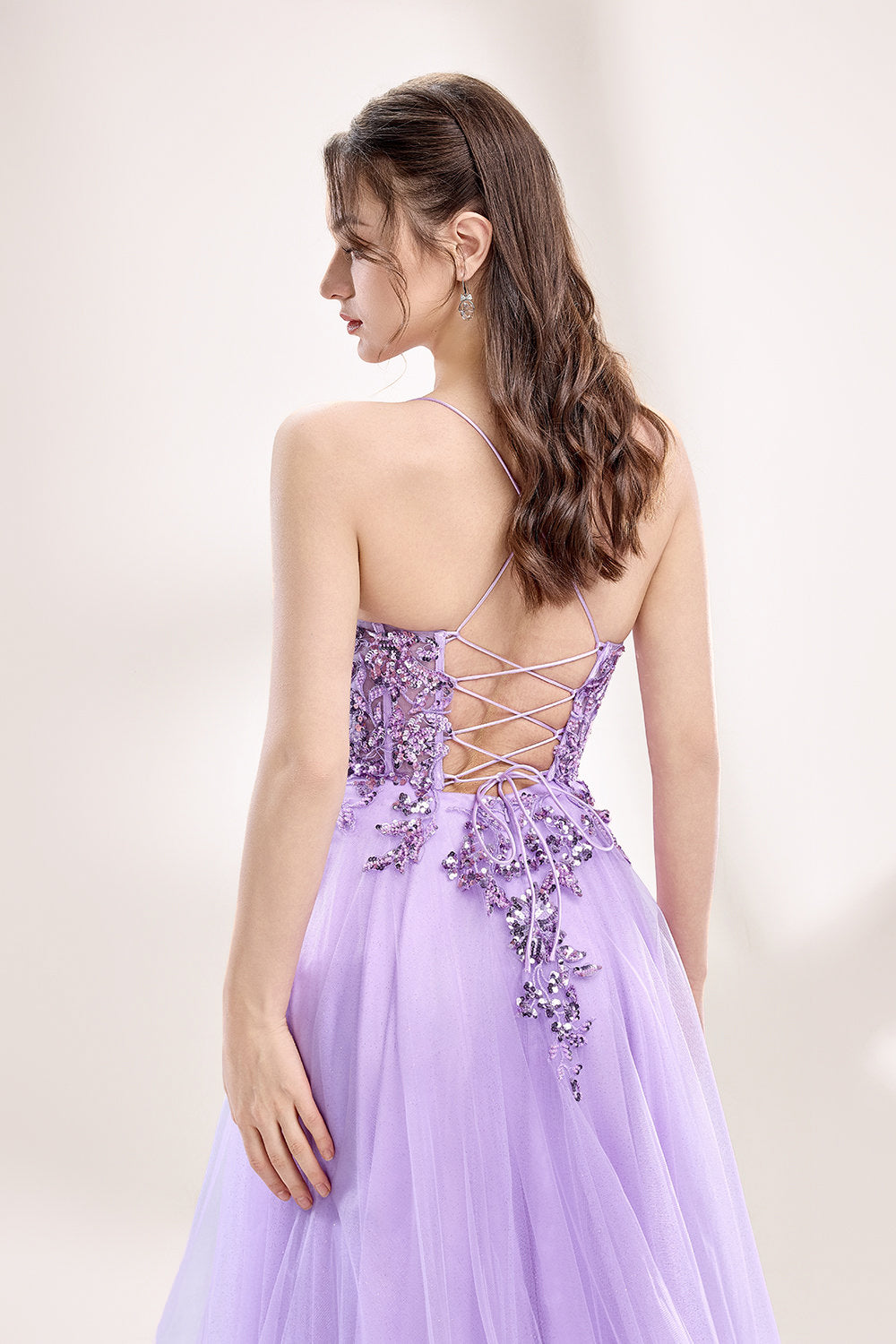 photograph of a young woman wearing a beautiful, floor-length, lavender ball gown with intricate sequin detailing on the bodice, sheer tulle skirt, spaghetti straps, long brown hair, fair skin, standing in a soft lit studio, neutral background, elegant, sophisticated, dreamy, fashion, glamour, full body shot, high quality, fashion photography, stylish, feminine, graceful, classy, modern, delicate, light, airy.33040-05