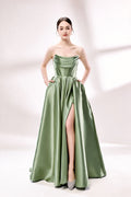 photo of a beautiful young woman standing in front of a white studio background, wearing a strapless, floor-length, olive green satin dress with a high slit on the right leg, hands in pockets, long brunette hair styled in a sleek bun, minimal makeup, elegant and classy look, silver high-heeled shoes, soft lighting, no other objects or people in the frame.33110B-01