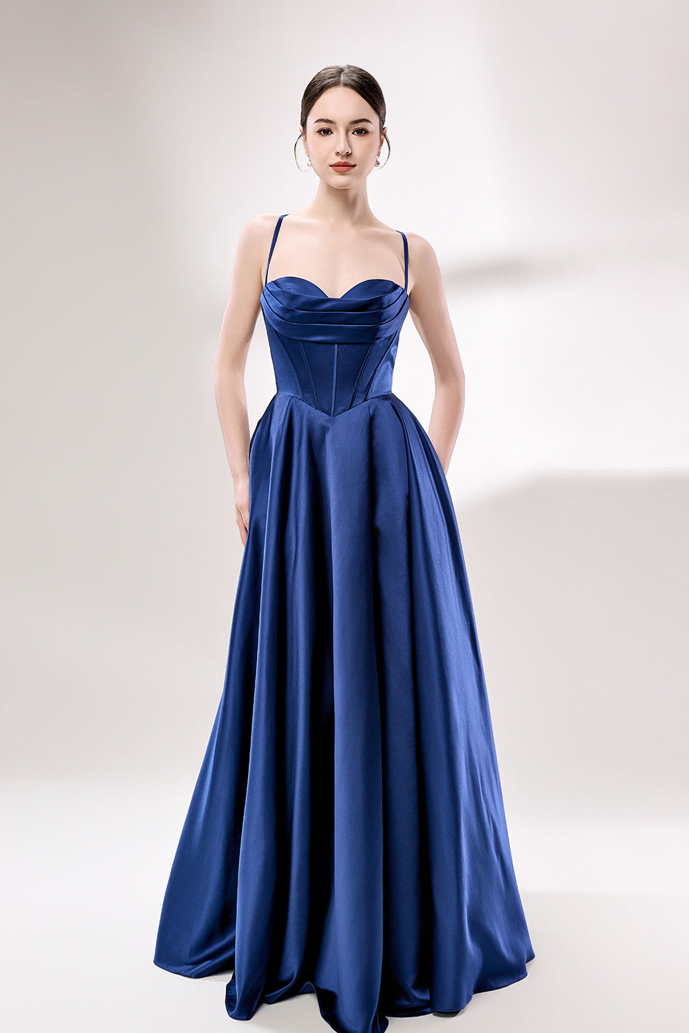 photo of a beautiful young woman, Asian descent, fair skin, long black hair in a low bun, wearing a stunning royal blue satin gown, corset-style top, full skirt, elegant and classy, standing against a plain white background, soft lighting, minimalistic setting, hands behind her back, confident pose, fashion photography, high-quality image, no watermarks.33119-01