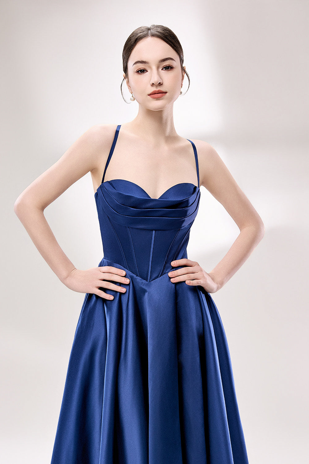 photo of a beautiful young woman, Asian descent, fair skin, long black hair in a low bun, wearing a stunning royal blue satin gown, corset-style top, full skirt, elegant and classy, standing against a plain white background, soft lighting, minimalistic setting, hands behind her back, confident pose, fashion photography, high-quality image, no watermarks.33119-03