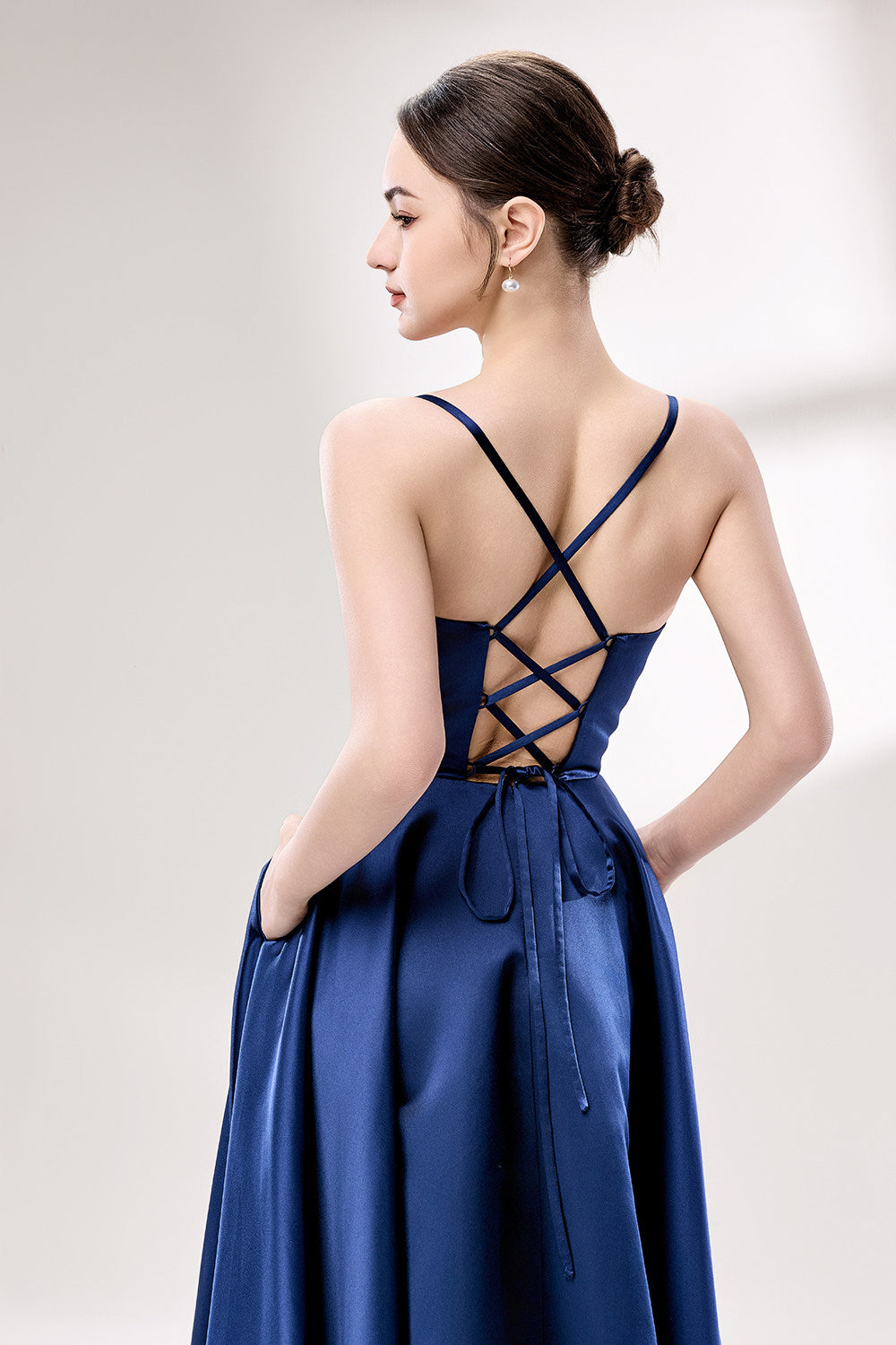 photo of a beautiful young woman, Asian descent, fair skin, long black hair in a low bun, wearing a stunning royal blue satin gown, corset-style top, full skirt, elegant and classy, standing against a plain white background, soft lighting, minimalistic setting, hands behind her back, confident pose, fashion photography, high-quality image, no watermarks.33119-05