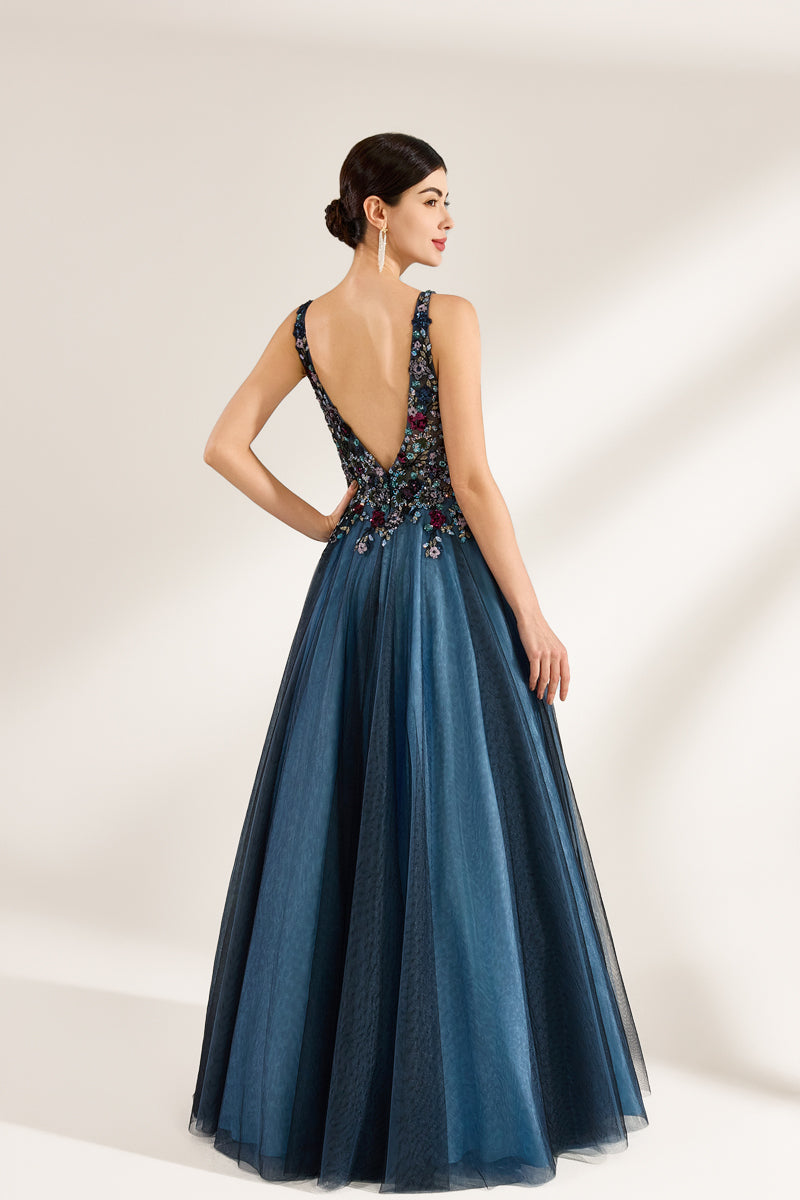 Photograph of a woman in an elegant, floor-length, backless gown. The dress features a deep V-back adorned with intricate floral embroidery in shades of red, blue, and green, complementing the blue tulle skirt. Her dark hair is styled in an elegant updo. She stands against a plain, off-white background, with soft, diffused lighting creating subtle shadows. The overall style is sophisticated and glamorous, suitable for formal events.