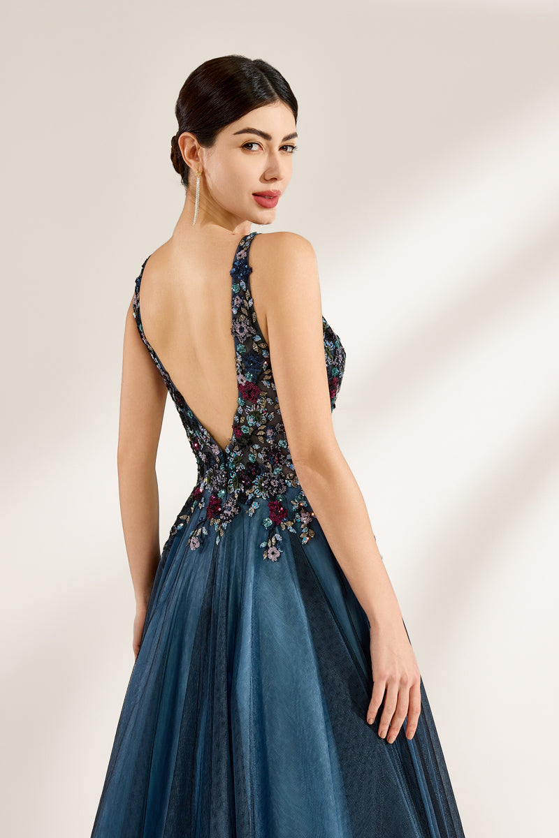 Photograph of a woman in an elegant, floor-length, backless gown. The dress features a deep V-back adorned with intricate floral embroidery in shades of red, blue, and green, complementing the blue tulle skirt. Her dark hair is styled in an elegant updo. She stands against a plain, off-white background, with soft, diffused lighting creating subtle shadows. The overall style is sophisticated and glamorous, suitable for formal events.