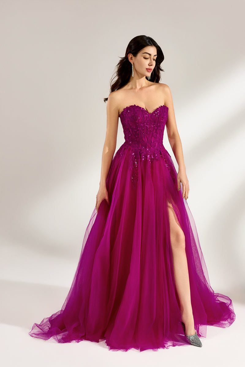 Photograph of a woman with long, dark hair in a strapless, vibrant magenta ball gown with a fitted bodice and a voluminous tulle skirt. The dress features a thigh-high slit on the left side and sparkling embellishments. She stands against a plain white background, exuding elegance and confidence.3321-01