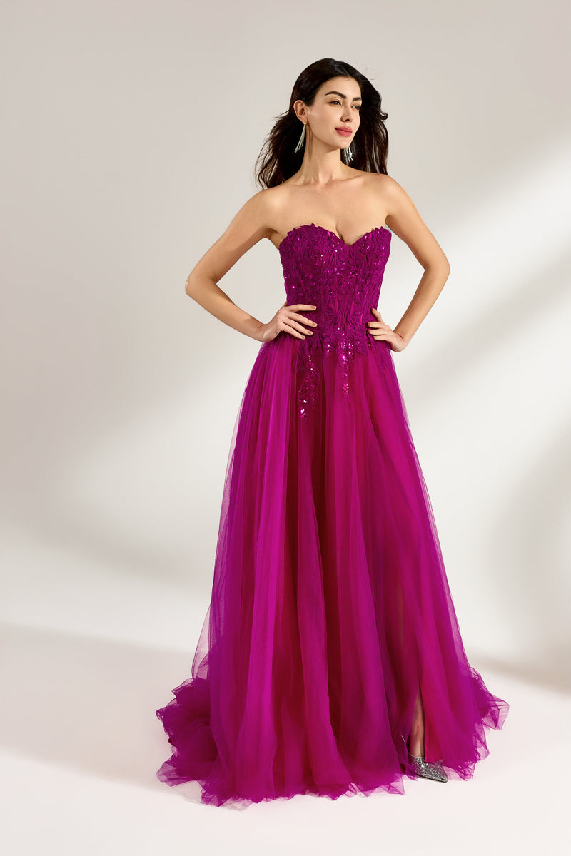 Photograph of a woman with long, dark hair in a strapless, vibrant magenta ball gown with a fitted bodice and a voluminous tulle skirt. The dress features a thigh-high slit on the left side and sparkling embellishments. She stands against a plain white background, exuding elegance and confidence.3321-03