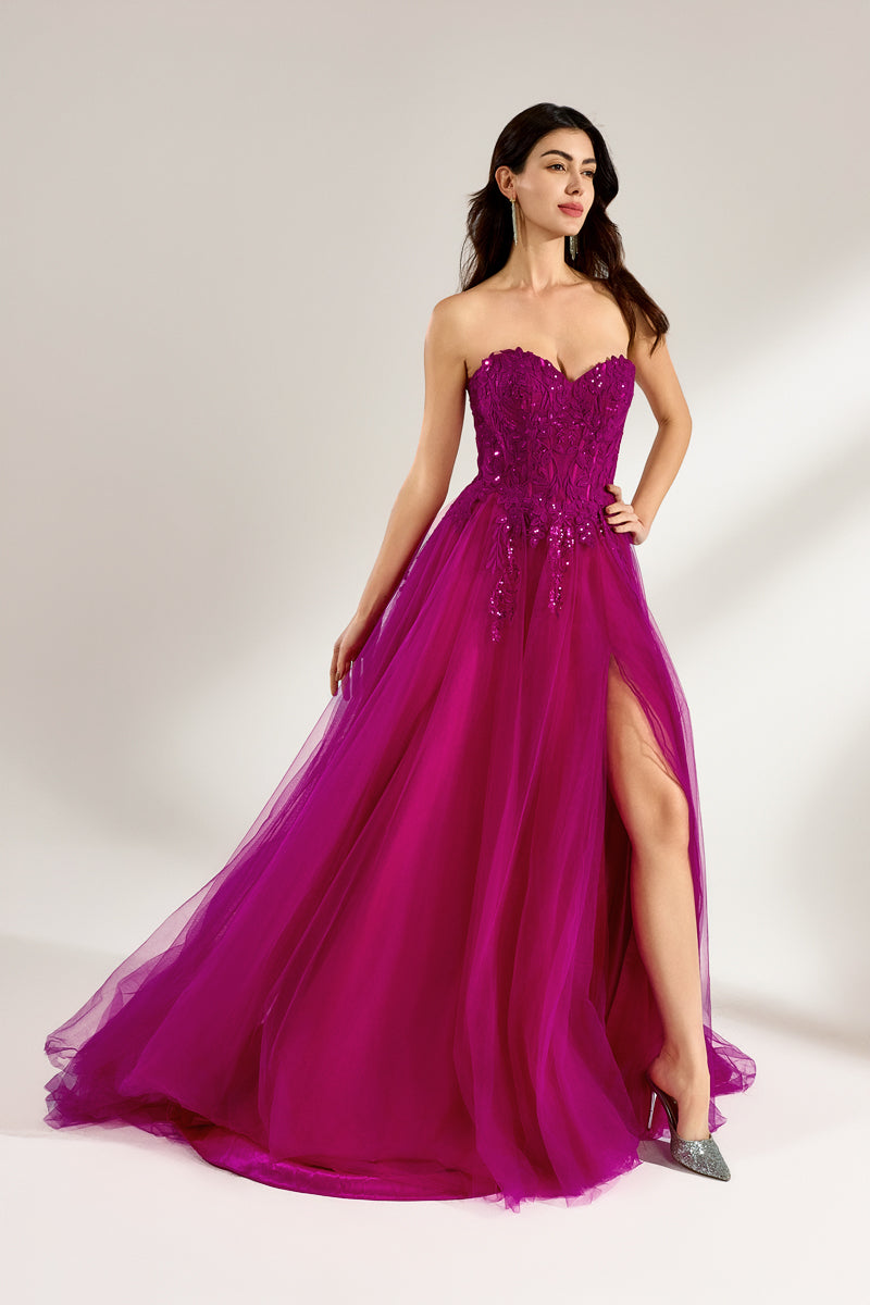 Photograph of a woman with long, dark hair in a strapless, vibrant magenta ball gown with a fitted bodice and a voluminous tulle skirt. The dress features a thigh-high slit on the left side and sparkling embellishments. She stands against a plain white background, exuding elegance and confidence.04