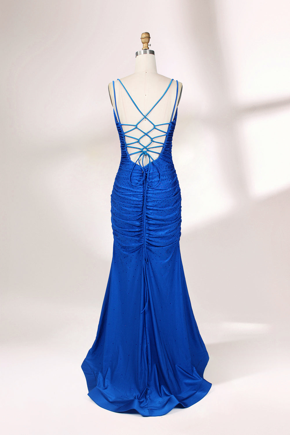 Photograph of a blue, floor-length evening gown displayed on a white dress form. The gown is sleeveless with a fitted bodice and a flared skirt, featuring thin shoulder straps and a textured, ruched design. The dress form is placed against a plain, off-white background, casting soft shadows.02