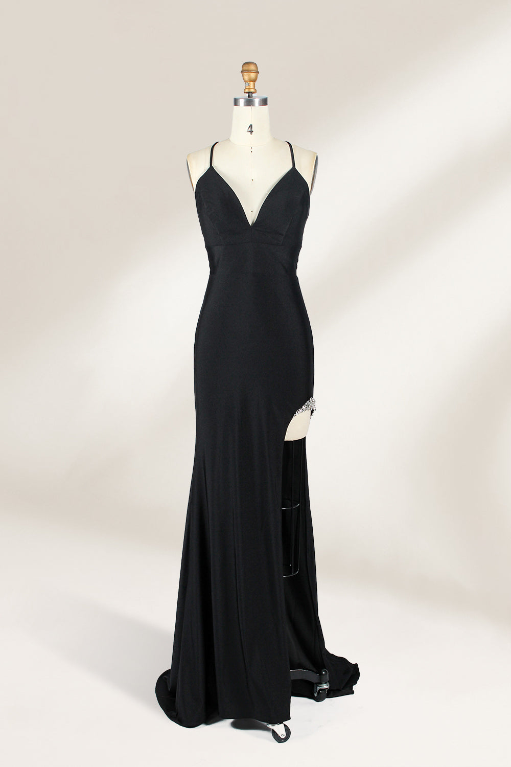 Displayed on a mannequin is a black evening gown. It features spaghetti straps, a deep V - neck, and a high slit with crystal detailing, creating a sleek and glamorous look for formal events.1