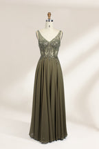 Photograph of an elegant, sleeveless, floor-length gown displayed on a dress form. The gown is a rich olive green with a fitted bodice adorned with intricate, sparkling embellishments. The neckline is a deep V, and the waistline is subtly cinched. The dress flows into a soft, gathered skirt. The background is a plain, light beige, enhancing the gown's luxurious texture and shimmering details.01