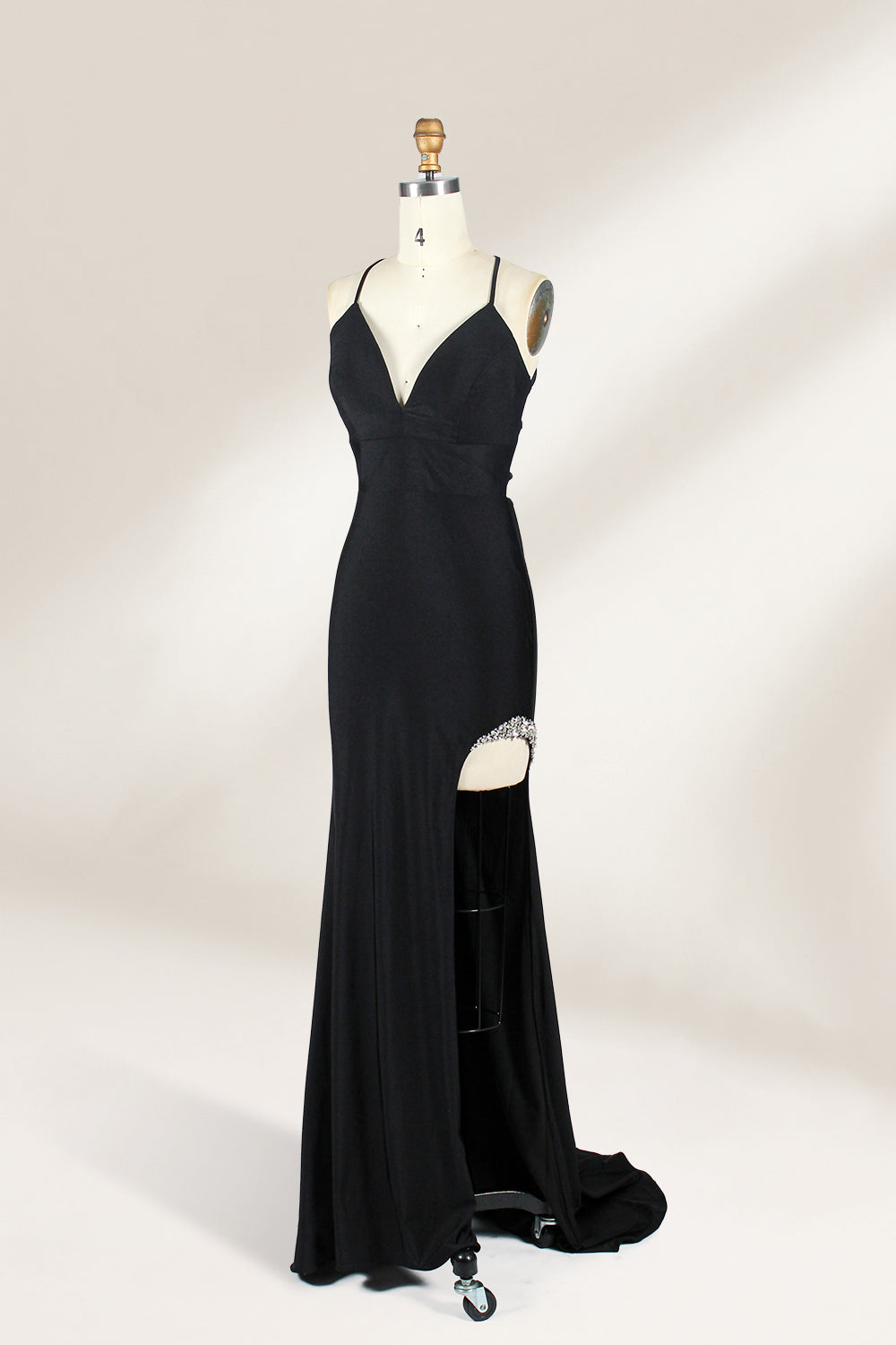 Displayed on a mannequin is a black evening gown. It features spaghetti straps, a deep V - neck, and a high slit with crystal detailing, creating a sleek and glamorous look for formal events.3