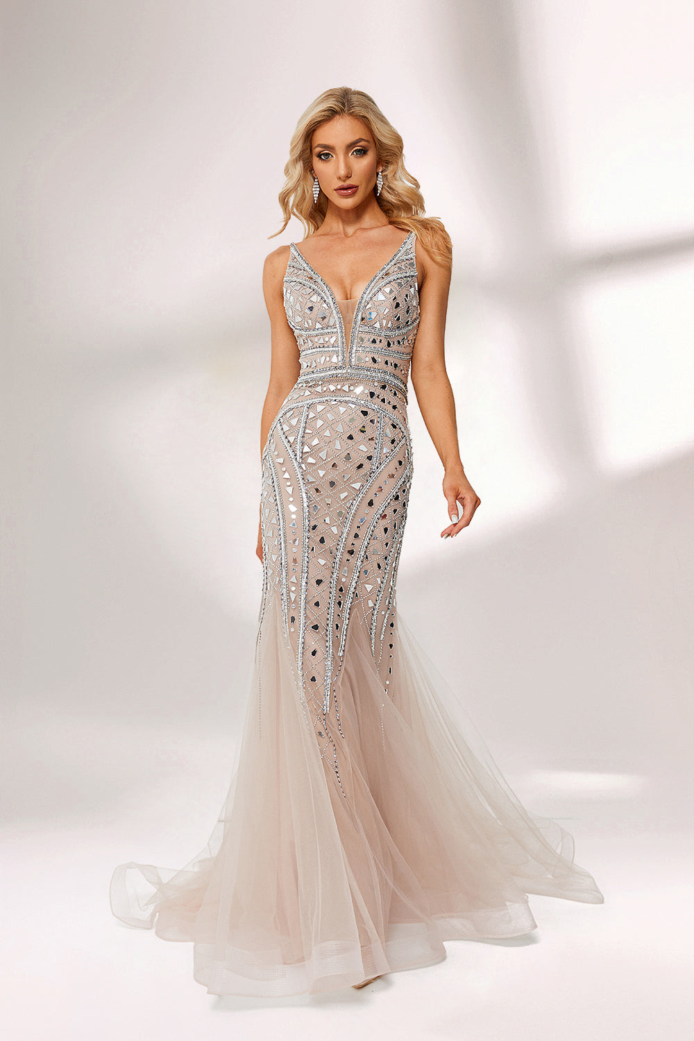 Bathed in soft light, a woman stuns in a nude - hued mermaid gown. It has thin straps, a deep V - neckline, and is covered with intricate silver geometric bead and sequin embroidery, plus a flowing tulle skirt. The shimmering details give off an opulent vibe, perfect for grand galas or red - carpet moments.4