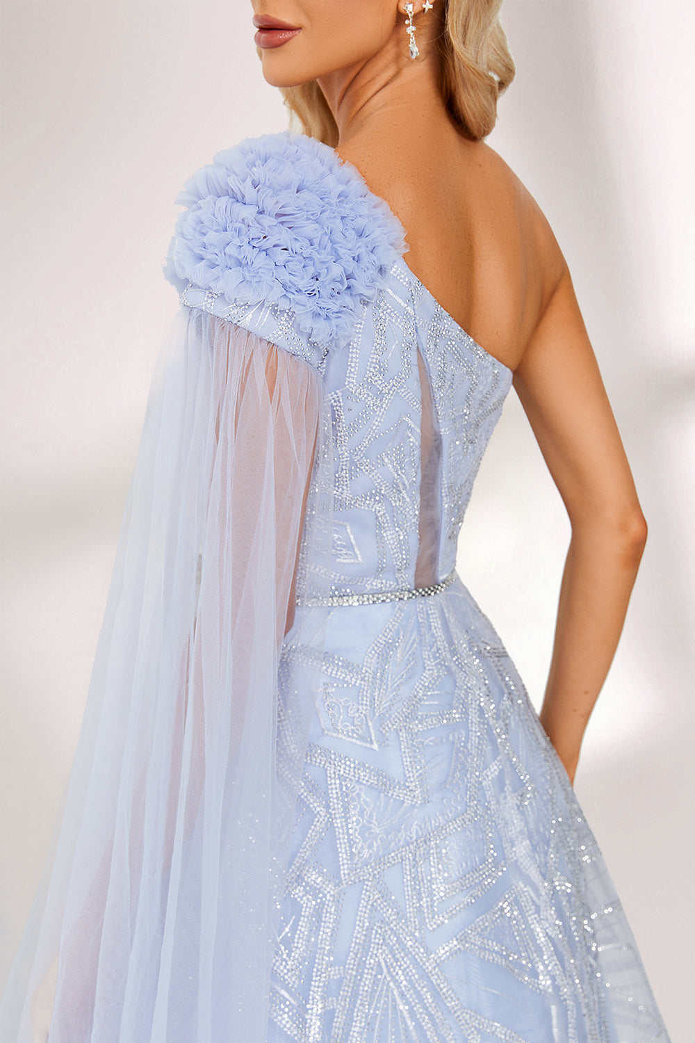In soft lighting, a woman stuns in a light blue one - shoulder evening gown. It has a floral accent on the shoulder, a sheer cape - like detail, and intricate silver embroidery. The dreamy design creates an elegant and fairy - tale - like look, perfect for grand events.6