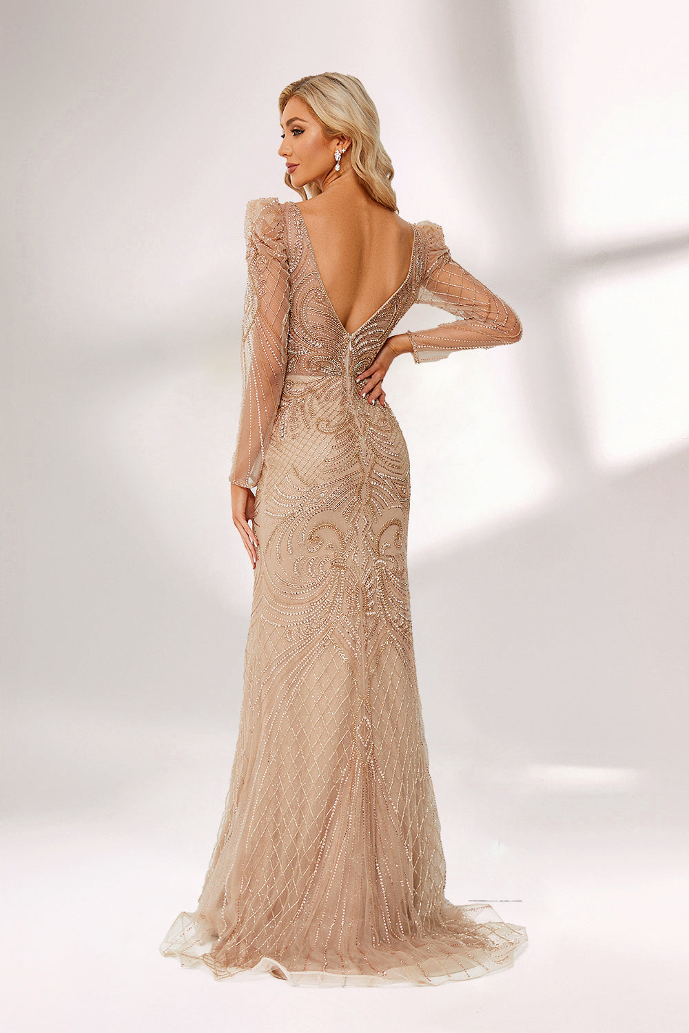 ：A woman stands against a light background, wearing a champagne - colored mermaid - style gown. It features a deep V - neckline, intricate beadwork throughout, and long sheer sleeves. The elegant design creates a glamorous and sophisticated look, perfect for formal events like galas or weddings.1