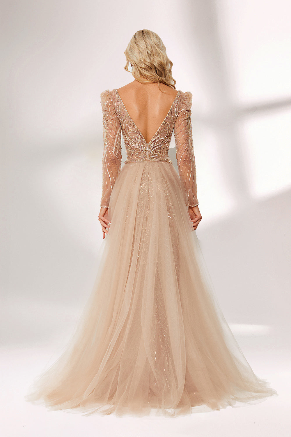 A woman stands against a light background, wearing a champagne - colored mermaid - style gown. It features a deep V - neckline, intricate beadwork throughout, and long sheer sleeves. The elegant design creates a glamorous and sophisticated look, perfect for formal events like galas or weddings.6