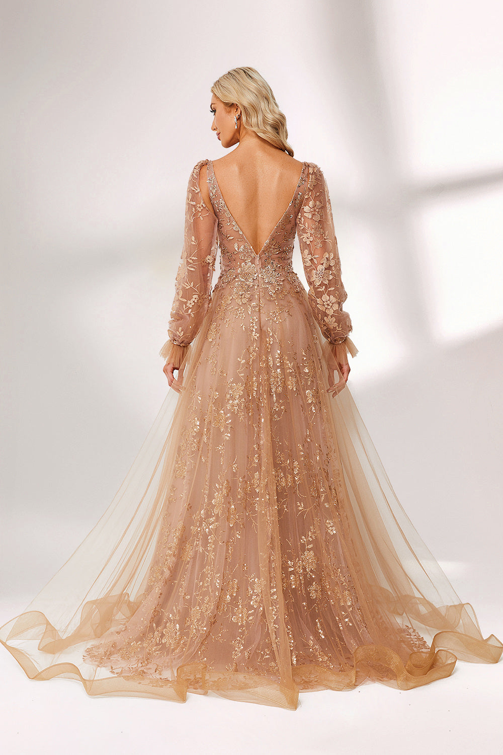 Set against a light backdrop, a woman is clad in a champagne - hued tulle gown. It boasts a deep V - neckline, long sheer sleeves adorned with lace embroidery, and a flowing tulle skirt featuring gold floral accents. The refined design exudes a romantic and luxurious charm, ideal for formal occasions such as proms or weddings.2