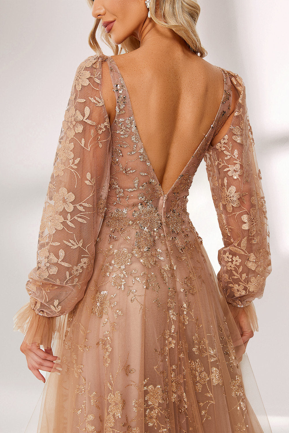 Set against a light backdrop, a woman is clad in a champagne - hued tulle gown. It boasts a deep V - neckline, long sheer sleeves adorned with lace embroidery, and a flowing tulle skirt featuring gold floral accents. The refined design exudes a romantic and luxurious charm, ideal for formal occasions such as proms or weddings.4