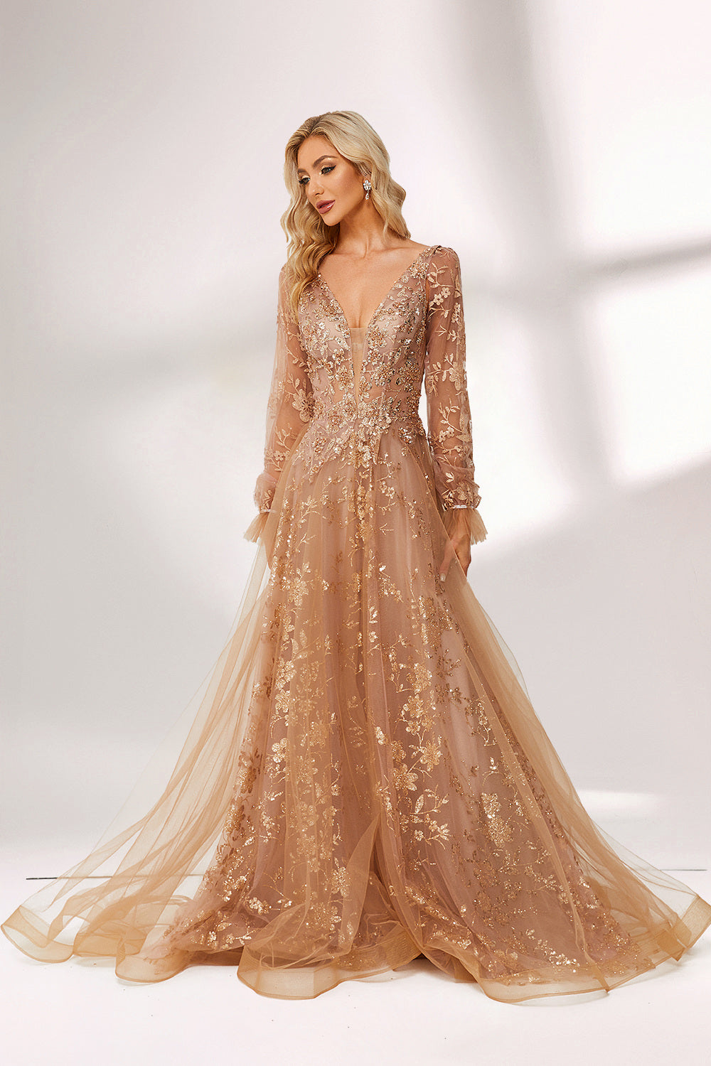 Set against a light backdrop, a woman is clad in a champagne - hued tulle gown. It boasts a deep V - neckline, long sheer sleeves adorned with lace embroidery, and a flowing tulle skirt featuring gold floral accents. The refined design exudes a romantic and luxurious charm, ideal for formal occasions such as proms or weddings.3