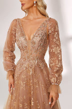 Set against a light backdrop, a woman is clad in a champagne - hued tulle gown. It boasts a deep V - neckline, long sheer sleeves adorned with lace embroidery, and a flowing tulle skirt featuring gold floral accents. The refined design exudes a romantic and luxurious charm, ideal for formal occasions such as proms or weddings.5