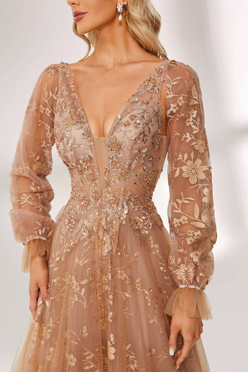 Set against a light backdrop, a woman is clad in a champagne - hued tulle gown. It boasts a deep V - neckline, long sheer sleeves adorned with lace embroidery, and a flowing tulle skirt featuring gold floral accents. The refined design exudes a romantic and luxurious charm, ideal for formal occasions such as proms or weddings.5