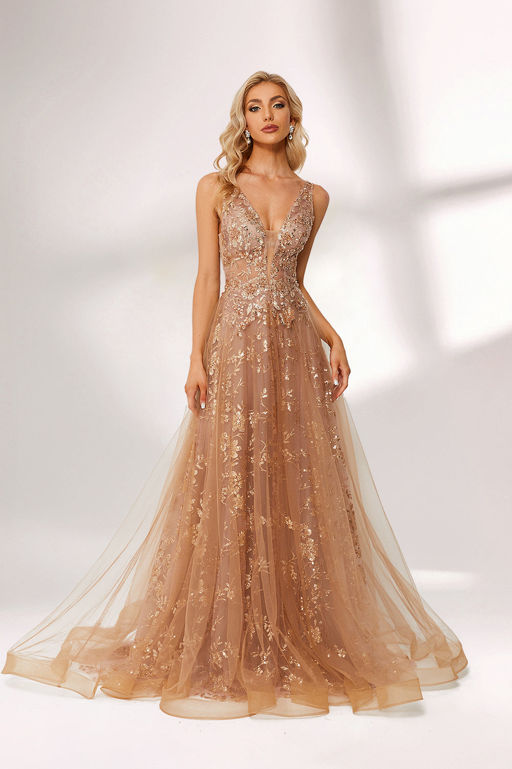 Set against a light backdrop, a woman is clad in a champagne - hued tulle gown. It boasts a deep V - neckline, long sheer sleeves adorned with lace embroidery, and a flowing tulle skirt featuring gold floral accents. The refined design exudes a romantic and luxurious charm, ideal for formal occasions such as proms or weddings.1