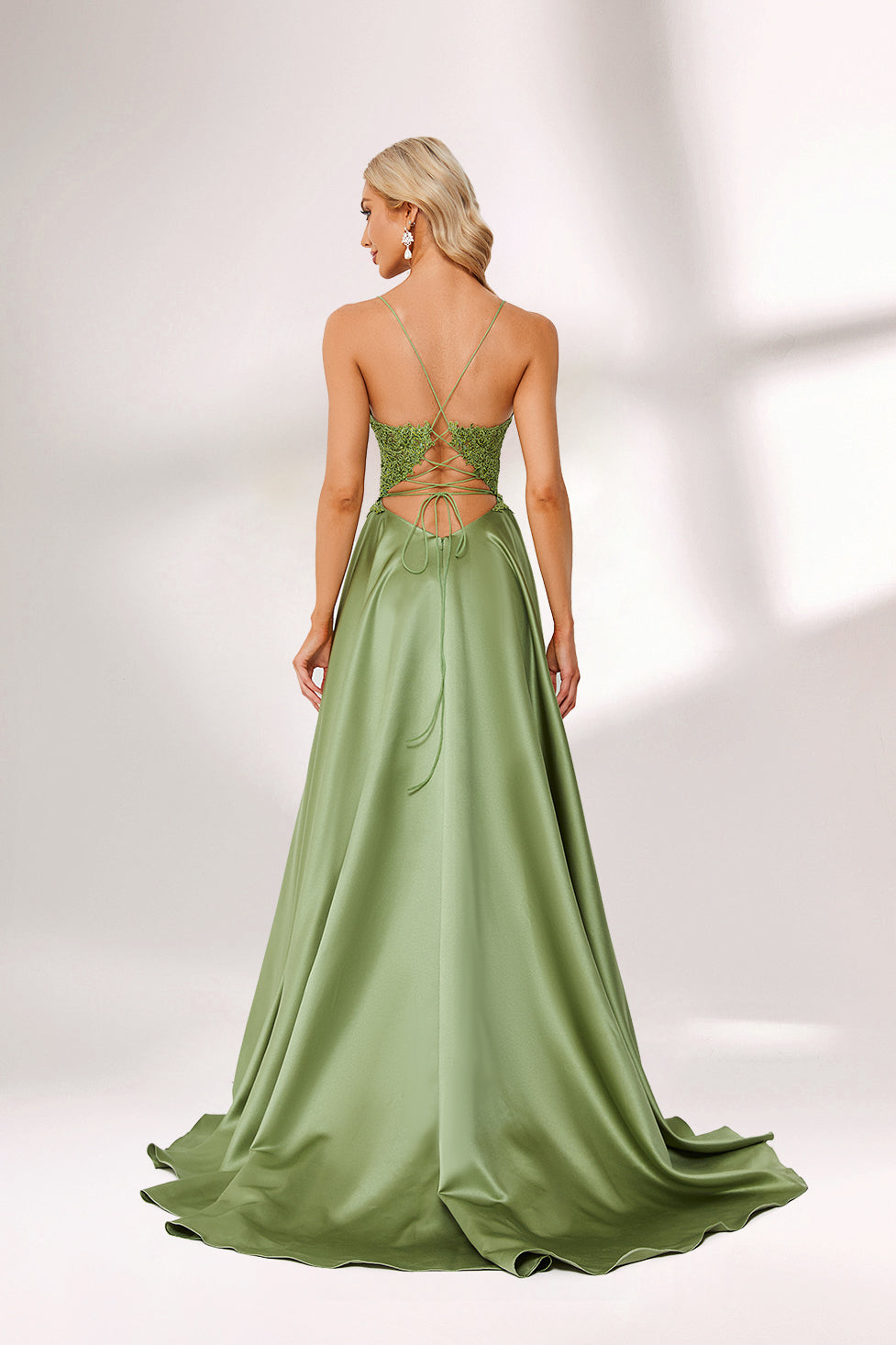 In soft lighting, a woman stuns in a green evening gown. It has spaghetti straps, a lace bodice, and a satin skirt with a slit, creating an elegant and alluring look for formal events.2
