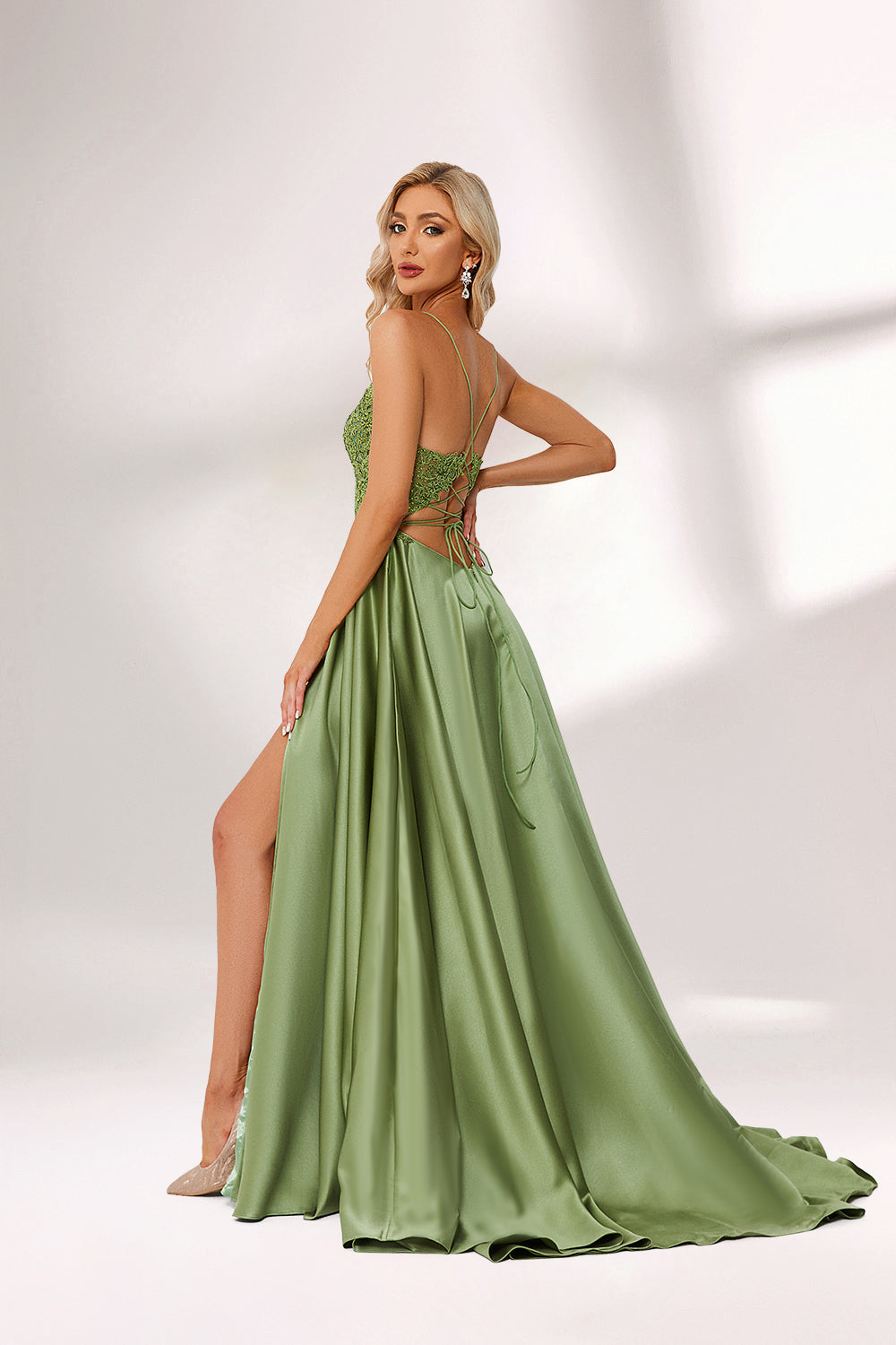 In soft lighting, a woman stuns in a green evening gown. It has spaghetti straps, a lace bodice, and a satin skirt with a slit, creating an elegant and alluring look for formal events.3