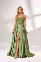 In soft lighting, a woman stuns in a green evening gown. It has spaghetti straps, a lace bodice, and a satin skirt with a slit, creating an elegant and alluring look for formal events.5