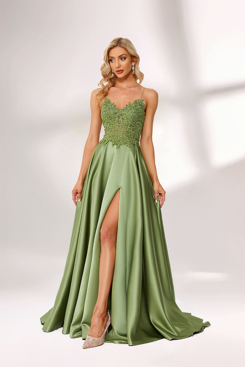 In soft lighting, a woman stuns in a green evening gown. It has spaghetti straps, a lace bodice, and a satin skirt with a slit, creating an elegant and alluring look for formal events.5