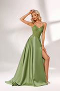 In soft lighting, a woman stuns in a green evening gown. It has spaghetti straps, a lace bodice, and a satin skirt with a slit, creating an elegant and alluring look for formal events.1