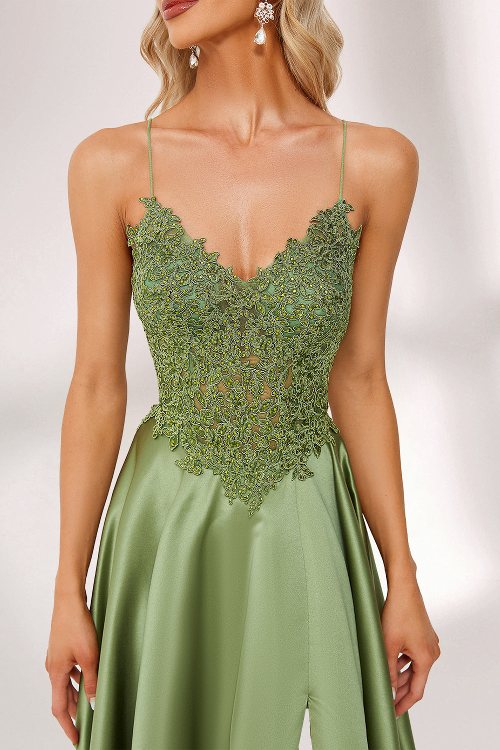 In soft lighting, a woman stuns in a green evening gown. It has spaghetti straps, a lace bodice, and a satin skirt with a slit, creating an elegant and alluring look for formal events.6