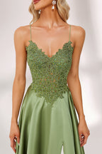 In soft lighting, a woman stuns in a green evening gown. It has spaghetti straps, a lace bodice, and a satin skirt with a slit, creating an elegant and alluring look for formal events.6
