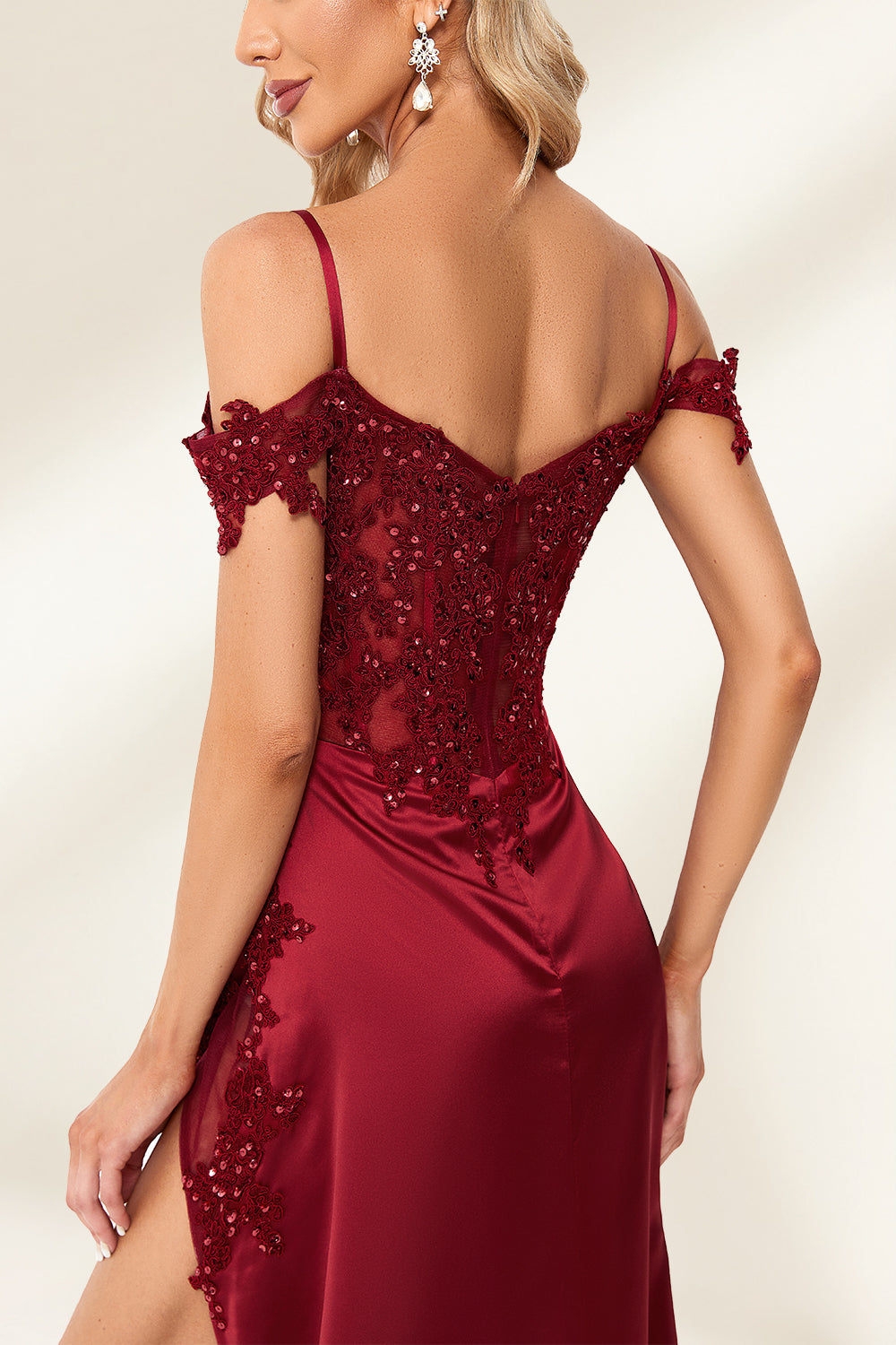 Photograph of a slender, attractive blonde woman with wavy hair. She wears a floor-length, off-shoulder, burgundy satin gown with a high slit and intricate beaded bodice. Her makeup is glamorous, with bold red lipstick. She stands against a plain white background, exuding elegance and sophistication.04