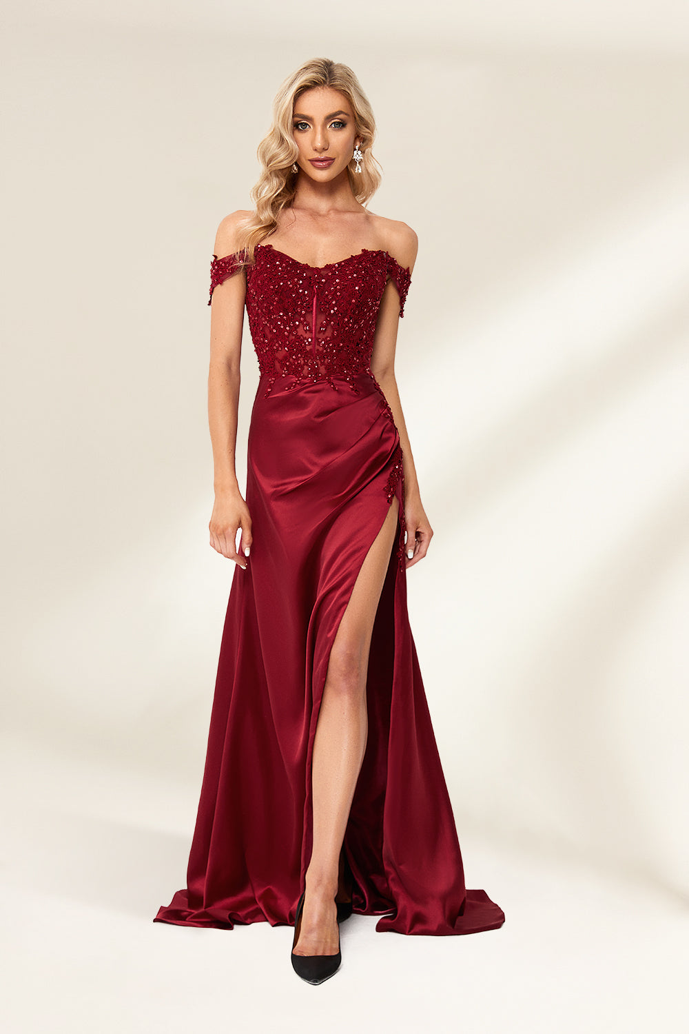 Photograph of a slender, attractive blonde woman with wavy hair. She wears a floor-length, off-shoulder, burgundy satin gown with a high slit and intricate beaded bodice. Her makeup is glamorous, with bold red lipstick. She stands against a plain white background, exuding elegance and sophistication.01