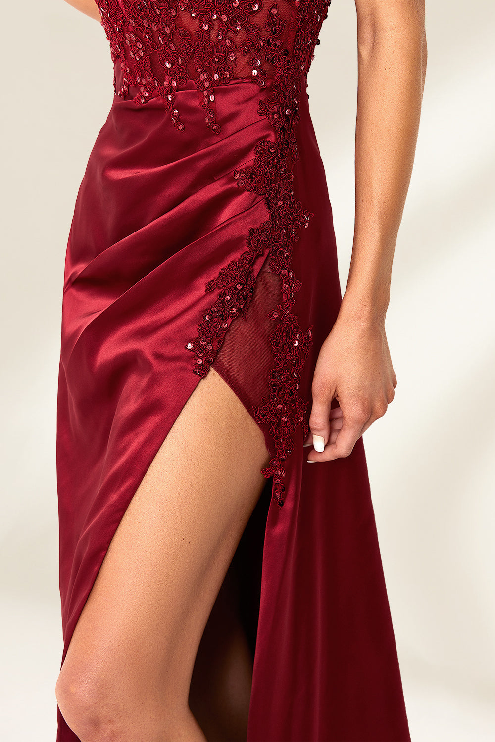 Photograph of a slender, attractive blonde woman with wavy hair. She wears a floor-length, off-shoulder, burgundy satin gown with a high slit and intricate beaded bodice. Her makeup is glamorous, with bold red lipstick. She stands against a plain white background, exuding elegance and sophistication.06