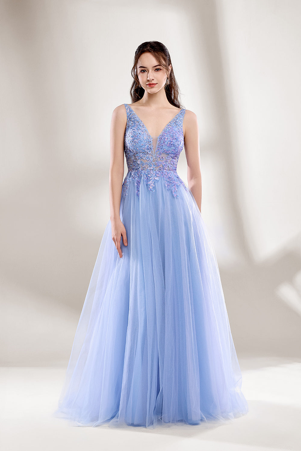 Bathed in soft light, a woman dazzles in a light blue tulle gown. It has a deep V - neckline with delicate lace embroidery on the bodice, and a flowing tulle skirt. The ethereal design creates a romantic and dreamy look, perfect for formal events like proms or weddings.1