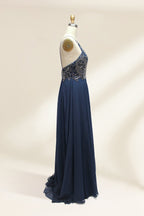 Photograph of a navy blue, floor-length, sleeveless gown on a dress form. The dress features intricate beadwork and sequin embellishments on the bodice, with a flowing, sheer skirt. The form is placed against a plain, light beige background, highlighting the dress's elegant, sophisticated design.9107-06