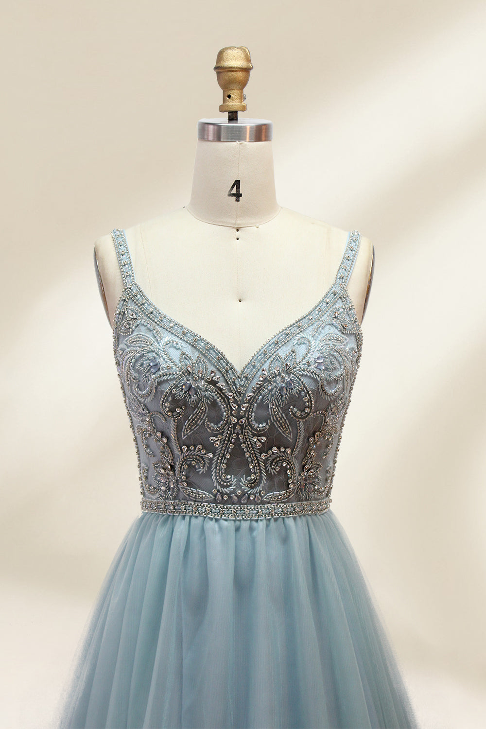 A photograph of a mannequin showcasing a floor-length, light blue tulle gown with intricate silver embroidery on the bodice. The gown has a fitted, sleeveless top and a voluminous skirt. The background is a plain, soft beige, highlighting the gown's elegant and sophisticated design.9133.1