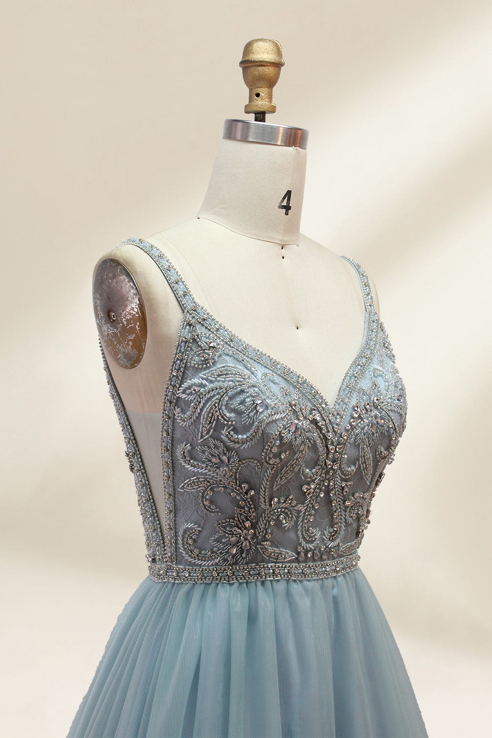 A photograph of a mannequin showcasing a floor-length, light blue tulle gown with intricate silver embroidery on the bodice. The gown has a fitted, sleeveless top and a voluminous skirt. The background is a plain, soft beige, highlighting the gown's elegant and sophisticated design.9133.2
