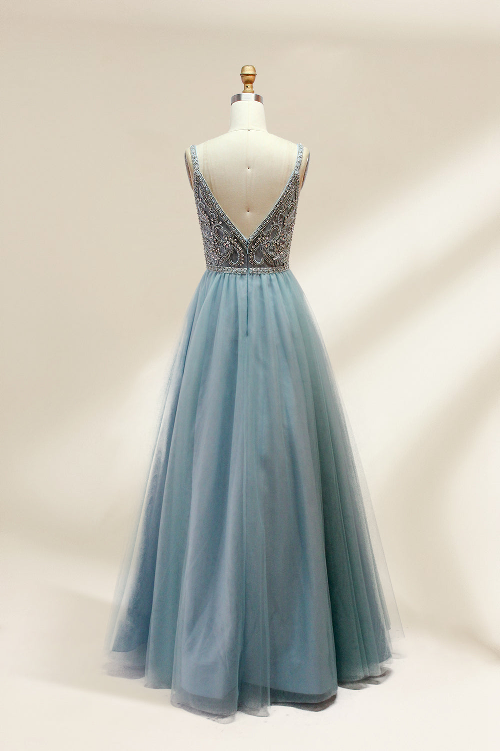 A photograph of a mannequin showcasing a floor-length, light blue tulle gown with intricate silver embroidery on the bodice. The gown has a fitted, sleeveless top and a voluminous skirt. The background is a plain, soft beige, highlighting the gown's elegant and sophisticated design.9133.4