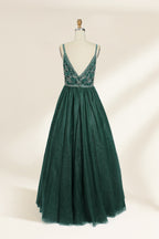 A photograph of a mannequin showcasing a floor-length, sleeveless, dark green evening gown. The gown features a V-neckline embellished with intricate beadwork and a fitted bodice that transitions into a voluminous tulle skirt. The background is plain and off-white, emphasizing the gown's elegant design.9133b.5