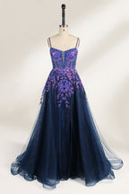 A photograph of a dark navy blue, floor-length evening gown displayed on a dress form. The gown features intricate floral embroidery in shades of purple and pink on the bodice, transitioning to a sheer, sparkling tulle skirt. The bodice is fitted with spaghetti straps, and the dress form is positioned against a plain, off-white background, highlighting the gown's elegant and luxurious design.1
