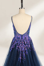 A photograph of a dark navy blue, floor-length evening gown displayed on a dress form. The gown features intricate floral embroidery in shades of purple and pink on the bodice, transitioning to a sheer, sparkling tulle skirt. The bodice is fitted with spaghetti straps, and the dress form is positioned against a plain, off-white background, highlighting the gown's elegant and luxurious design.6