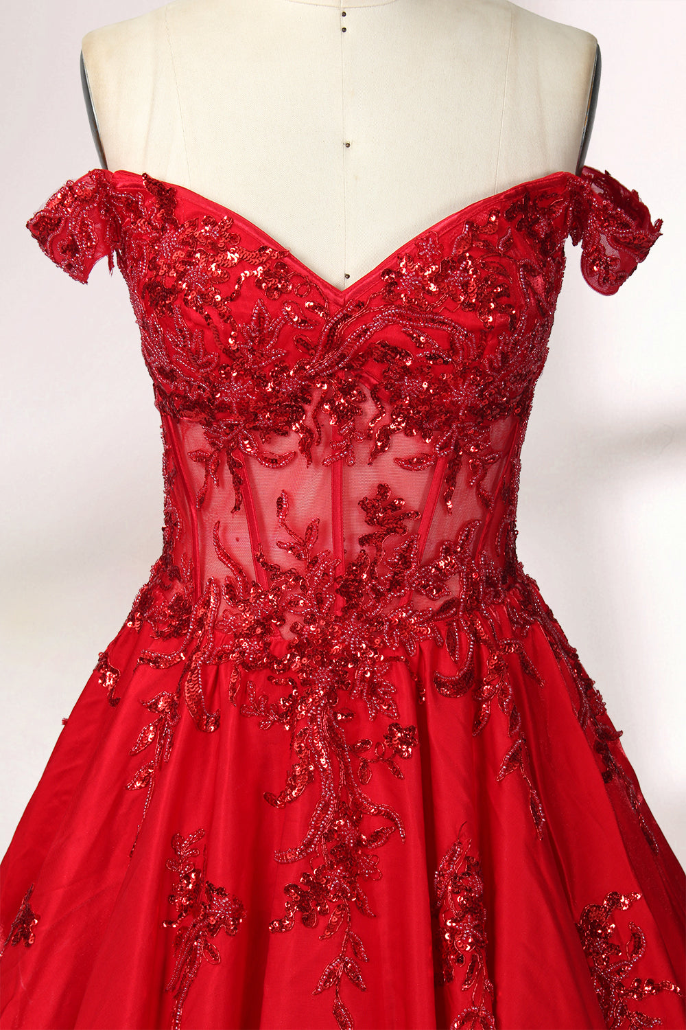 Photograph of an elegant, off-the-shoulder red ball gown on a white dress form. The dress features intricate, sparkling beadwork on the bodice and a voluminous, flowing skirt adorned with delicate floral patterns. The background is a plain white studio setup with soft shadows, emphasizing the dress's vibrant color and luxurious texture.03