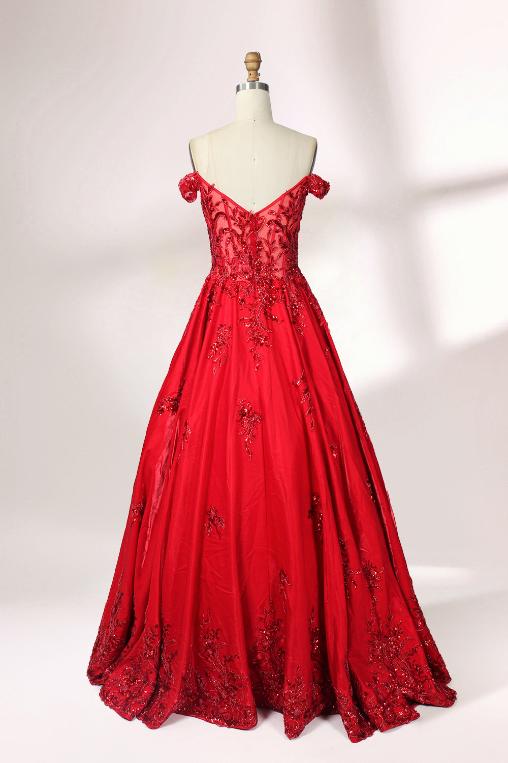 Photograph of an elegant, off-the-shoulder red ball gown on a white dress form. The dress features intricate, sparkling beadwork on the bodice and a voluminous, flowing skirt adorned with delicate floral patterns. The background is a plain white studio setup with soft shadows, emphasizing the dress's vibrant color and luxurious texture.02