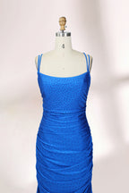 Photograph of a blue, floor-length evening gown displayed on a white dress form. The gown is sleeveless with a fitted bodice and a flared skirt, featuring thin shoulder straps and a textured, ruched design. The dress form is placed against a plain, off-white background, casting soft shadows.04