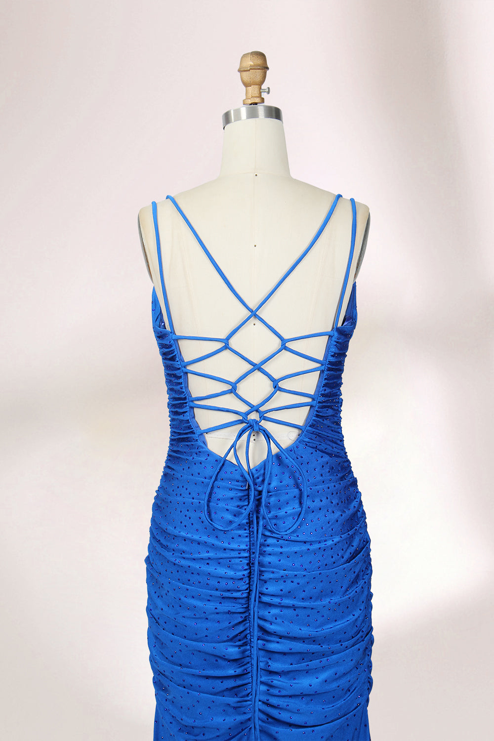 Photograph of a blue, floor-length evening gown displayed on a white dress form. The gown is sleeveless with a fitted bodice and a flared skirt, featuring thin shoulder straps and a textured, ruched design. The dress form is placed against a plain, off-white background, casting soft shadows.06
