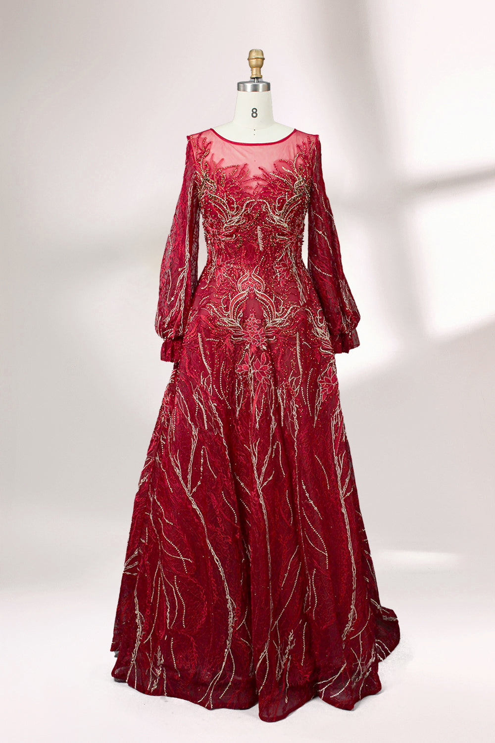 Presented on a mannequin is a deep - red evening gown. It features a sheer neckline, long billowy sleeves, and intricate gold - toned embroidery throughout. The elaborate design gives off a luxurious and elegant vibe, ideal for formal occasions.1