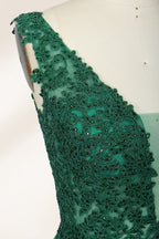 Photograph of a mannequin wearing a floor-length, deep V-neck emerald green satin gown with intricate lace detailing around the neckline and bodice. The gown features a fitted bodice and a flowing, pleated skirt. The mannequin stands on a wooden base against a plain, light beige background, highlighting the gown's elegant and luxurious design.06