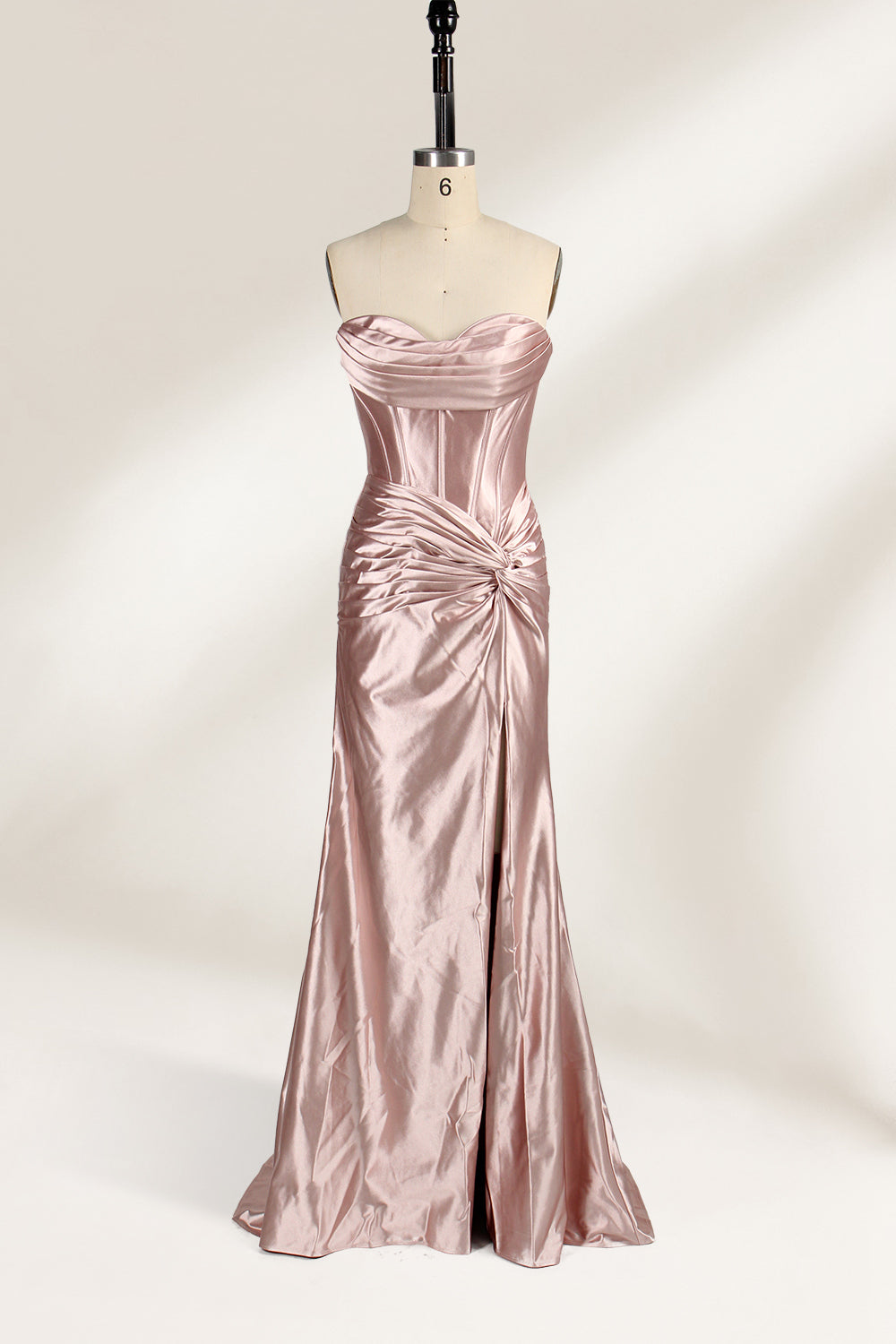 A mannequin showcases a strapless, blush - pink satin gown against a light backdrop. It features a ruched bodice with a draped neckline and a twisted detail at the waist, along with a mermaid silhouette and a side slit. The smooth satin fabric exudes elegance, perfect for formal events like galas.6